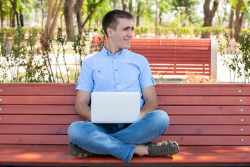 Fototapeta premium Young man with laptop sitting on a wooden bench