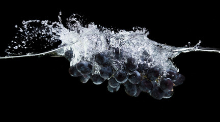 Fresh purple grapes in clear water with splash