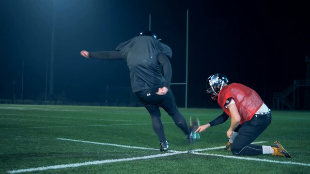American football ball is getting kicked out from between the ground and player's hand