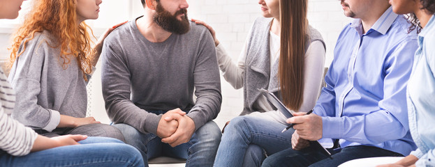 Women comforting stressed man at support therapy - obrazy, fototapety, plakaty