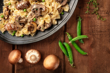Obraz na płótnie Canvas Mushroom and cheese pasta. Farfalle with cremini and green peas, shot from the top with ingredients on a dark rustic wooden background with a place for text