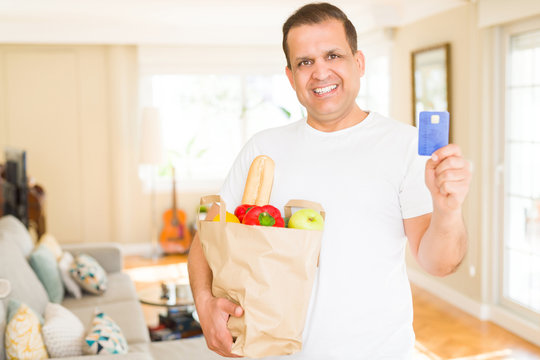 Middle age man holding groceries bag and showing credit card