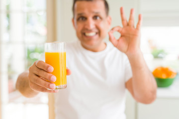 Fototapeta premium Middle age man drinking a glass of orange juice at home doing ok sign with fingers, excellent symbol