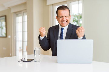 Middle age business man working with computer laptop very happy and excited doing winner gesture with arms raised, smiling and screaming for success. Celebration concept.