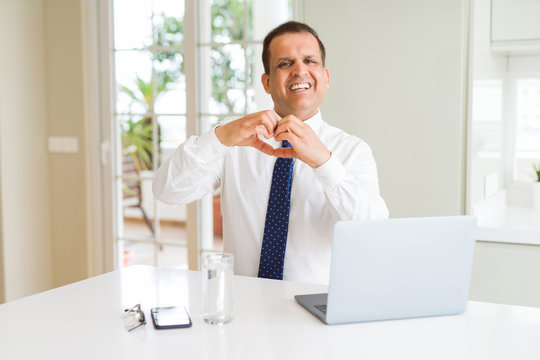 Middle age business man working with computer laptop smiling in love showing heart symbol and shape with hands. Romantic concept.