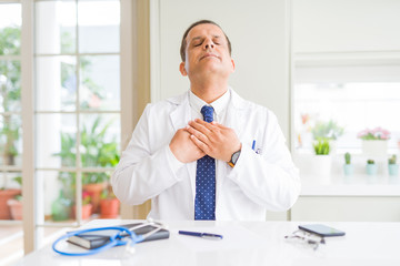 Middle age doctor man wearing medical coat at the clinic smiling with hands on chest with closed eyes and grateful gesture on face. Health concept.