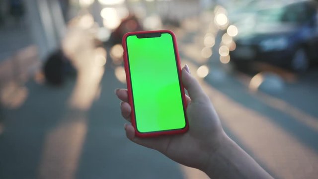 Close-up view of person holding a smartphone swiping pages on mockup greenscreen outdoor. Girl browsing social networks online on a mobile phone in the street at sunlight.