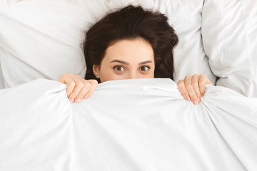 Playful girl peeking out of blanket, hiding in bed