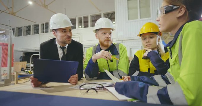 Workers and manager in safety helmets working with documents at factory