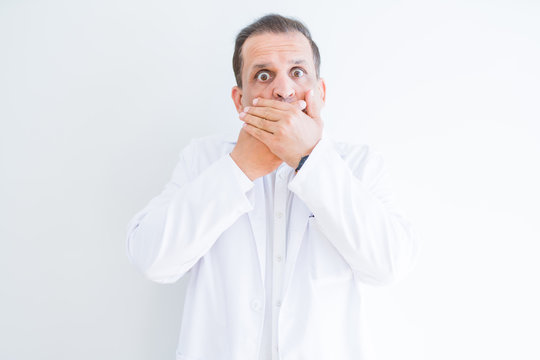 Middle age doctor man wearing medical coat over white background shocked covering mouth with hands for mistake. Secret concept.