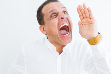 Middle age man shouting crazy with hands over mouth over white wall background