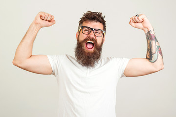 Screaming bearded brutal man with hands up. Excited bearded man in glasses celebrating success....