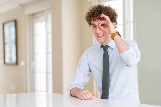 Young business man wearing a tie doing ok gesture with hand smiling, eye looking through fingers with happy face.