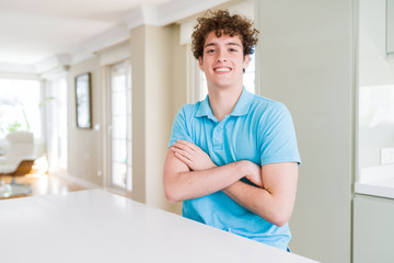 Young handsome man wearing casual blue t-shirt at home happy face smiling with crossed arms looking at the camera. Positive person.