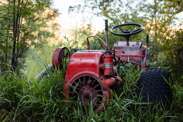 Abandoned red tractor wreck, overgrown with long green grass on a farm.