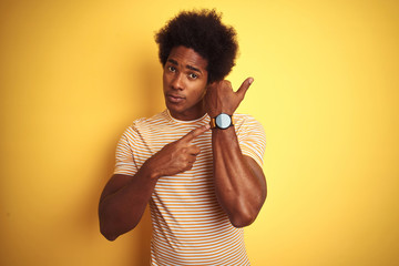 American man with afro hair wearing striped t-shirt standing over isolated yellow background In...