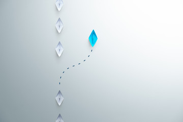 Group of white paper ship in one direction and one blue paper ship pointing in different way on...
