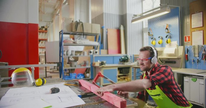 Caucasian Man Working Cutting Plank With Handsaw And Listening To Music Using Headphones. Having Fun At Work