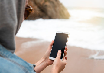Mockup image, close-up of hipster girl holding mobile smartphone in hands and shooting beautiful seaview. Tourist, traveler using mobile on the beach. 