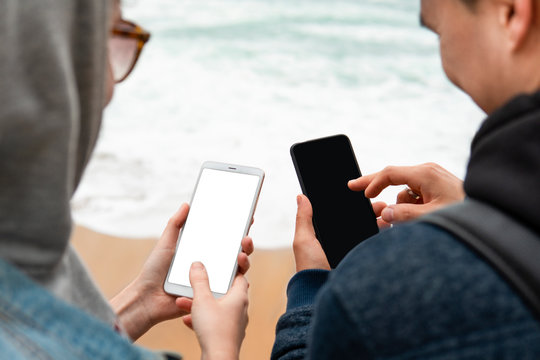 Mockup image, close-up of hipster couple holding mobile smartphones in hands and shooting beautiful sea view. Tourists sharing photos of the beautiful seascape and blue ocean, lifestyle travel        