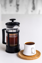 Cup of coffee made with French press is ready to serve, white background.