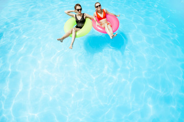Two women swimming on the inflatable rings, relaxing in the water pool outdoors during the summer time, View from above