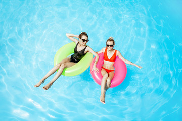 Two women swimming on the inflatable rings, relaxing in the water pool outdoors during the summer time, View from above
