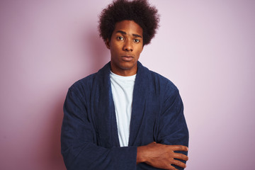 Young african american man wearing pajama standing over isolated pink background skeptic and...
