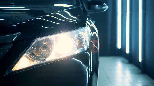 Switched-on headlight of a black car in a close up