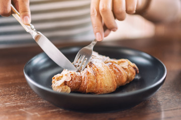 Closeup image of a woman eating a piece of croissant by knife and fork