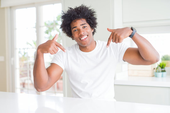 Young african american man wearing casual white t-shirt sitting at home looking confident with smile on face, pointing oneself with fingers proud and happy.