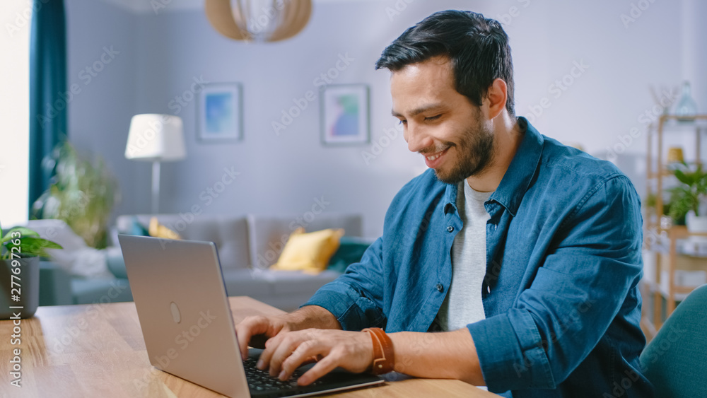 Poster portrait of handsome young man using laptop computer at home, watching and smiling at a content. coz