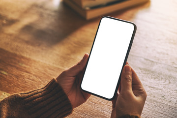 Mockup image of hands holding black mobile phone with blank desktop screen on wooden table