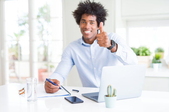 African American business man working writing on notebook happy with big smile doing ok sign, thumb up with fingers, excellent sign