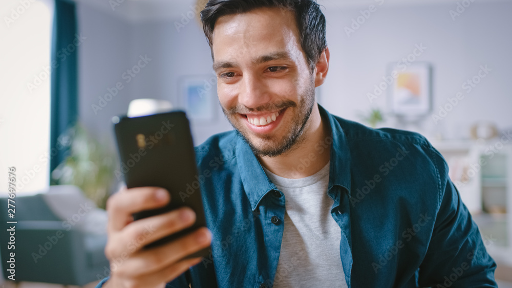 Poster handsome smiling man uses smartphone while relaxing in his living room. guy browsing in internet, us