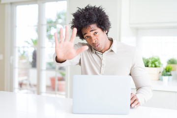 African American man working using laptop with open hand doing stop sign with serious and confident expression, defense gesture