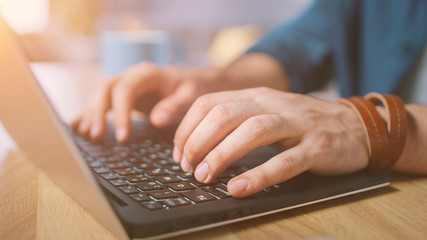 Close-up Shot of a Man Typing on a Laptop at Home / Office. Shot Made with Warm Sun Light.