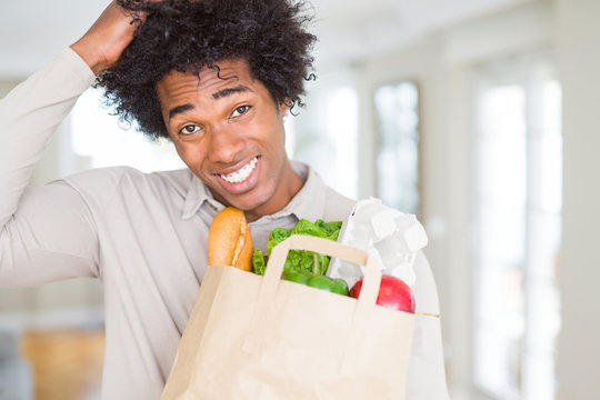 African American man holding groceries bag with fresh vegetables at home stressed with hand on head, shocked with shame and surprise face, angry and frustrated. Fear and upset for mistake.