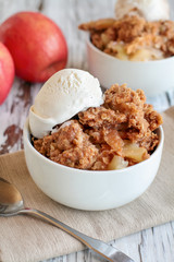 Fresh hot homemade apple crisp or crumble with crunchy streusel topping topped with vanilla bean ice cream. Selective focus with blurred background. 