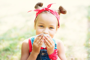 Little girl wipes her mouth with a napkin. A child with a hair tail and a red bandana.