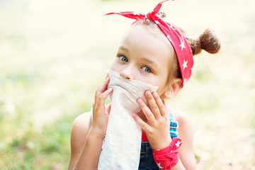 Obraz premium Little girl wipes her mouth with a napkin. A child with a hair tail and a red bandana.