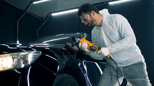 Front side of an automobile is being polished by a mechanic