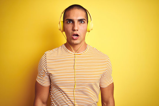 Young handsome man using headphones over yellow isolated background afraid and shocked with surprise expression, fear and excited face.