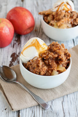 Fresh hot homemade apple crisp or crumble with crunchy streusel topping topped with vanilla bean ice cream and Caramel Sauce. Selective focus with blurred background