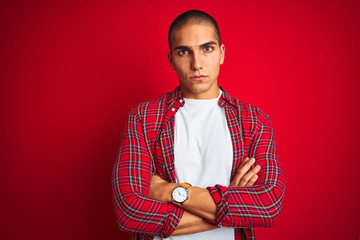 Young handsome man wearing a shirt using watch over red isolated background skeptic and nervous, disapproving expression on face with crossed arms. Negative person.