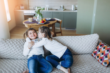 Portrait of little caucasian adorable girls playing together in cozy bedroom smiling and relaxing in scandinavian design style. Happiness, leisure, children lifestyle, childhood, education concept