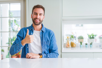 Handsome man at home doing happy thumbs up gesture with hand. Approving expression looking at the camera showing success.