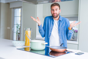 Handsome man cooking italian spaghetti pasta at the kitchen clueless and confused expression with...