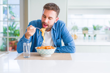 Handsome man eating pasta with meatballs and tomato sauce at home while smiling at the camera