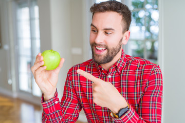 Handsome man eating fresh healthy green apple very happy pointing with hand and finger